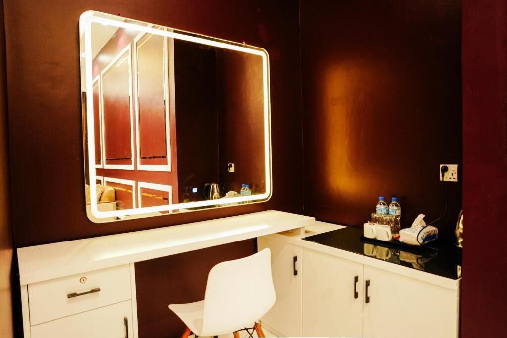 A bathroom with a vanity, a mirror with lights, a white chair, and toiletries on the counter.