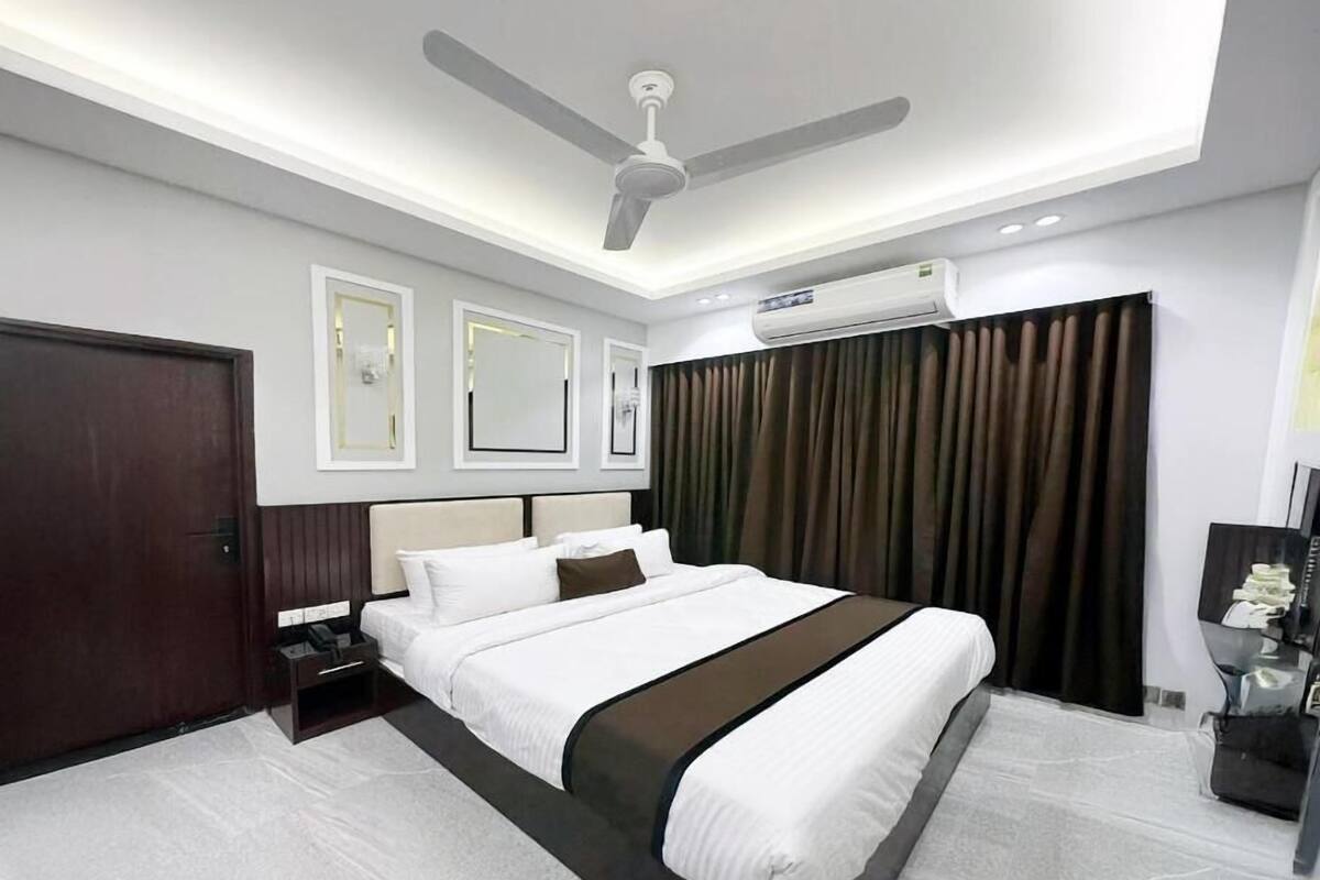 A modern hotel room with a large bed, ceiling fan, air conditioning unit, and a dark curtain.