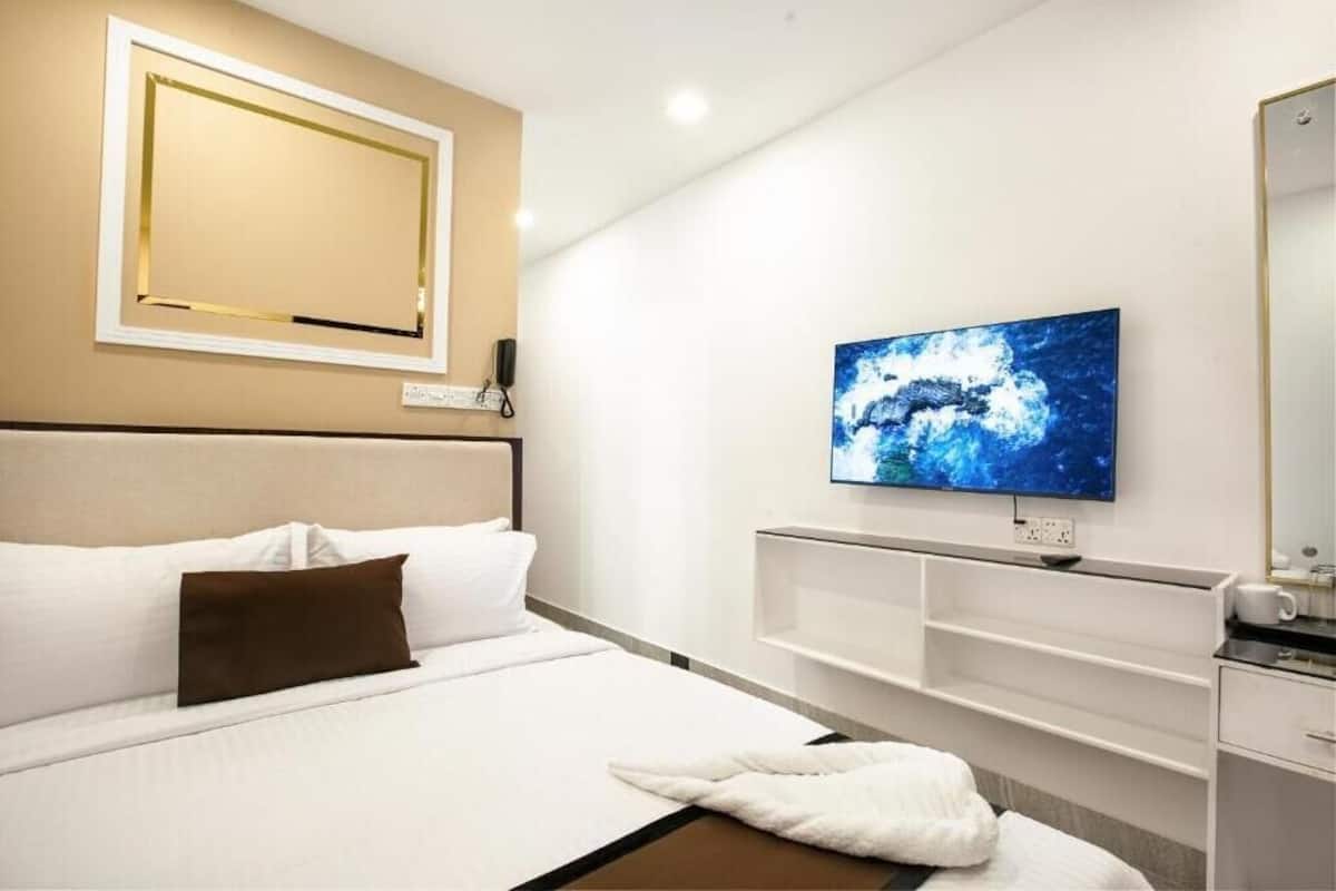 A modern hotel room with a large bed, a flat-screen TV mounted on the wall, a bedside table, and a built-in shelf unit.