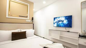 A modern hotel room with a large bed, a flat-screen TV mounted on the wall, a bedside table, and a built-in shelf unit.