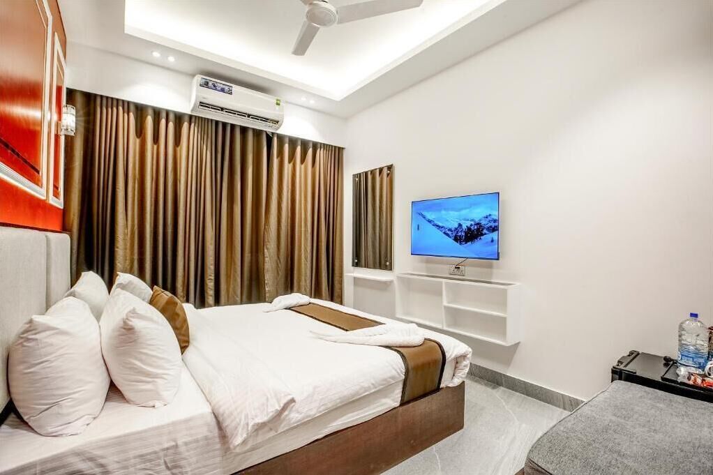 A modern hotel room with a bed, a television, a ceiling fan, and an air conditioning unit.