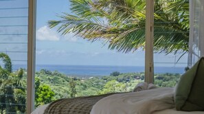 A bedroom with a large window overlooking a lush landscape and the ocean. - Elysian (Terranora)