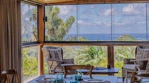 Un coin repas aménagé avec des meubles en osier et une table pour deux, offrant une vue panoramique sur l’océan et une végétation luxuriante.