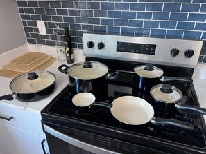 A kitchen with a black stove, pots with lids, a cutting board, and a bottle of olive oil.