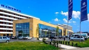 Un edificio moderno con facciata in vetro, con la scritta 'HARTLEY' e un parcheggio con diverse automobili.