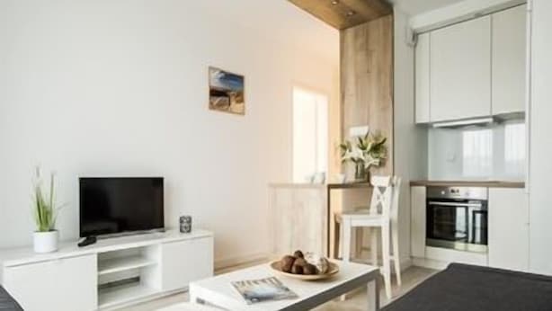 Un soggiorno moderno con una TV a schermo piatto, un mobile TV bianco, un divano, un tavolino da caffè e un angolo cottura con fornello e forno.