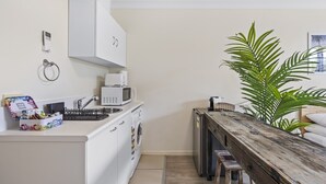 A compact kitchen with a microwave, sink, and a wooden table. - Comfy Studio Apartment in Marcoola Beach (Sunshine Coast)