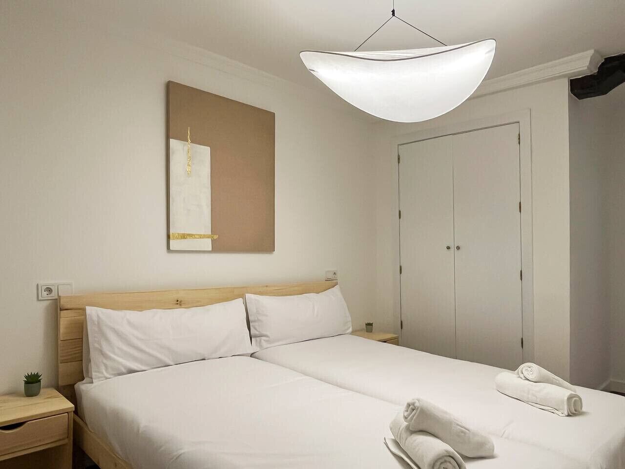 A hotel room with a double bed, a bedside table with a lamp, a wall-mounted artwork, and a wardrobe.