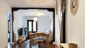 Ein geräumiges Zimmer mit Holzboden, einem Esstisch mit Stühlen, einem Bett mit Holzgestell und einem großen Fenster.