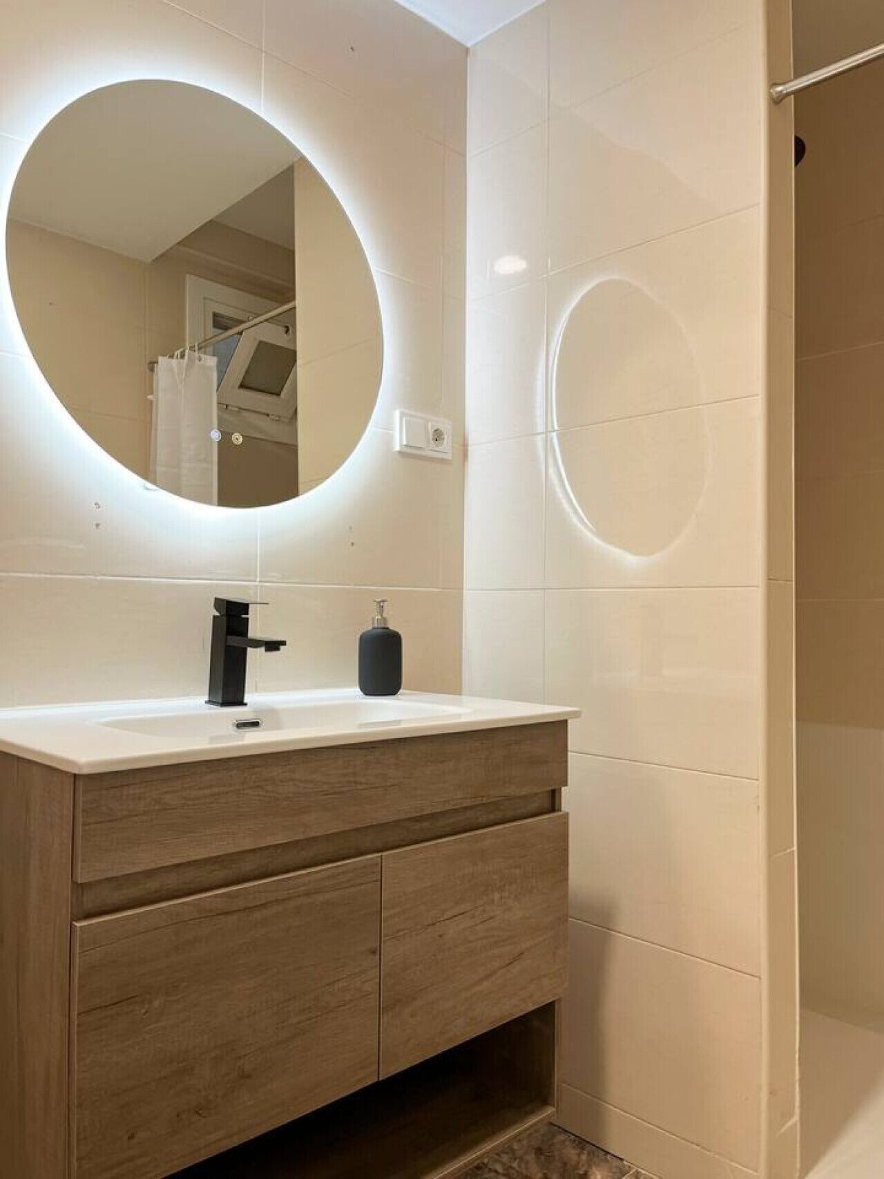 Een moderne badkamer met een ronde spiegel, een wit wastafelmeubel en houten kastjes.