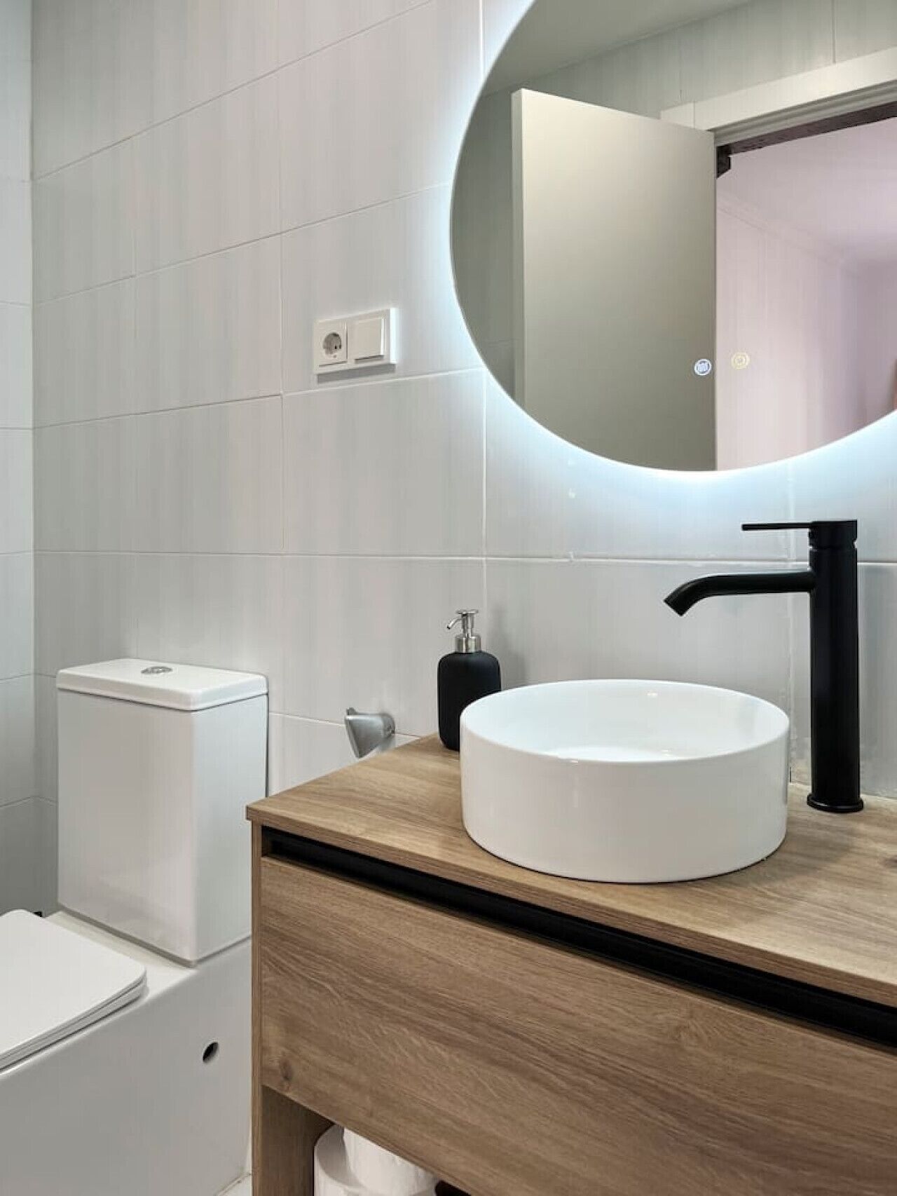Un baño moderno con un espejo redondo, un lavabo blanco y un mueble de tocador de madera.
