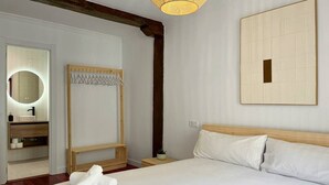 Ein ordentlich eingerichtetes Hotelzimmer mit einem großen Bett, einem Holz-Kopfteil, einem Nachttisch mit Pflanze und einem Spiegel über dem Waschbecken.