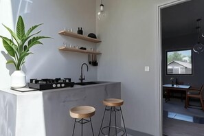 A modern kitchen with a marble countertop, two stools, a potted plant, and wooden shelves.