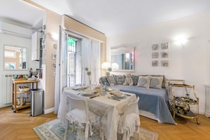 A well-lit room with a dining table set for four, a sofa with a blue cover, and a decorative cart.