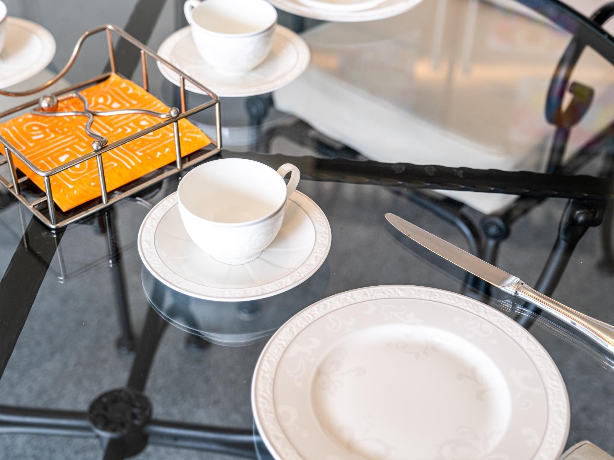 A dining table with white plates, a cup, a knife, and a yellow tray with a geometric pattern.