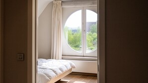 Una camera da letto con un letto, una finestra tonda e vista sul verde all'esterno.