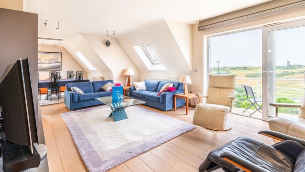 Un soggiorno moderno in stile loft con un grande televisore, divani blu, un tavolino da caffè in vetro e vista sulla campagna.