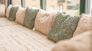 Un siège de fenêtre agrémenté d’une rangée de coussins et offrant une vue sur les bâtiments environnants.