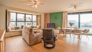 Un salon moderne comprenant un canapé, un fauteuil inclinable, une table à manger avec des chaises, un téléviseur et une grande fenêtre avec des rideaux.