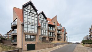 Un immeuble moderne à plusieurs étages, doté de grandes fenêtres et de balcons, situé le long d’une rue pavée.