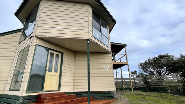 Un immeuble de deux étages doté d’un balcon, avec le numéro « 37 » bien visible, et une clôture verte en arrière-plan.