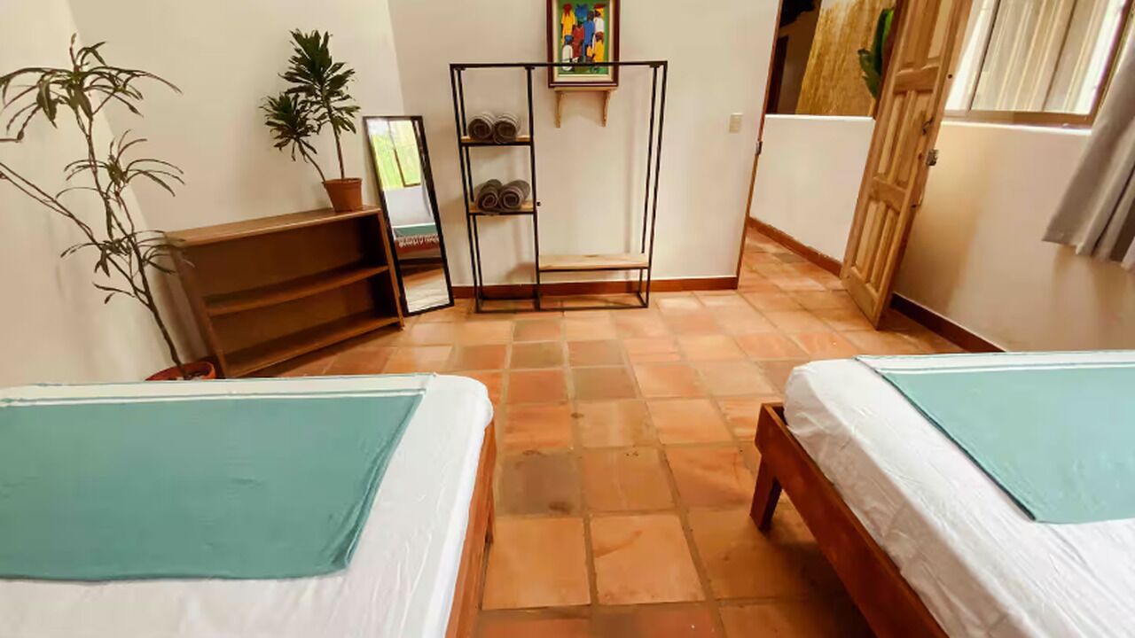 Ein Zimmer mit zwei Betten, einer hölzernen Bank, einem Metallregal und einer Topfpflanze.