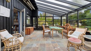 Un patio cubierto con mobiliario de mimbre, una mesa y una estantería.