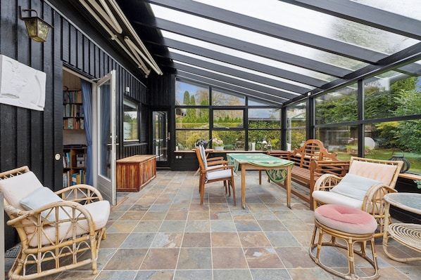 A covered patio with wicker furniture, a table, and a bookshelf.