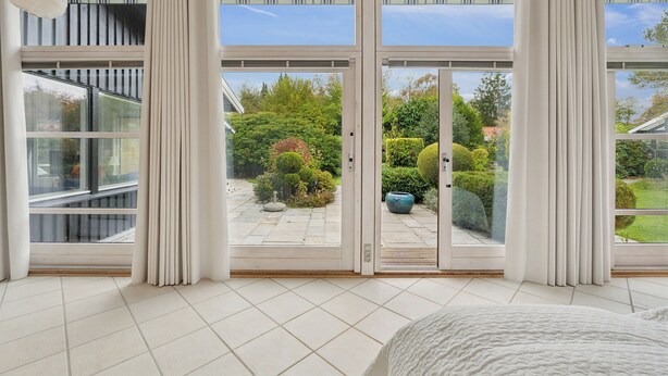 Una habitación moderna con grandes puertas correderas de vidrio que dan a un jardín, una cama y vistas al exterior.
