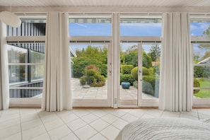 A modern room with large sliding glass doors leading to a garden, a bed, and a view of the outside.