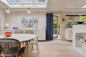 A modern kitchen with a dining area, wooden walls, and a large window with a view of greenery.
