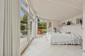 A bedroom with a large sliding glass door, a bed with white bedding, a red chair, and a small table. - Lovely holiday home near Hornbæk (Hornbæk)