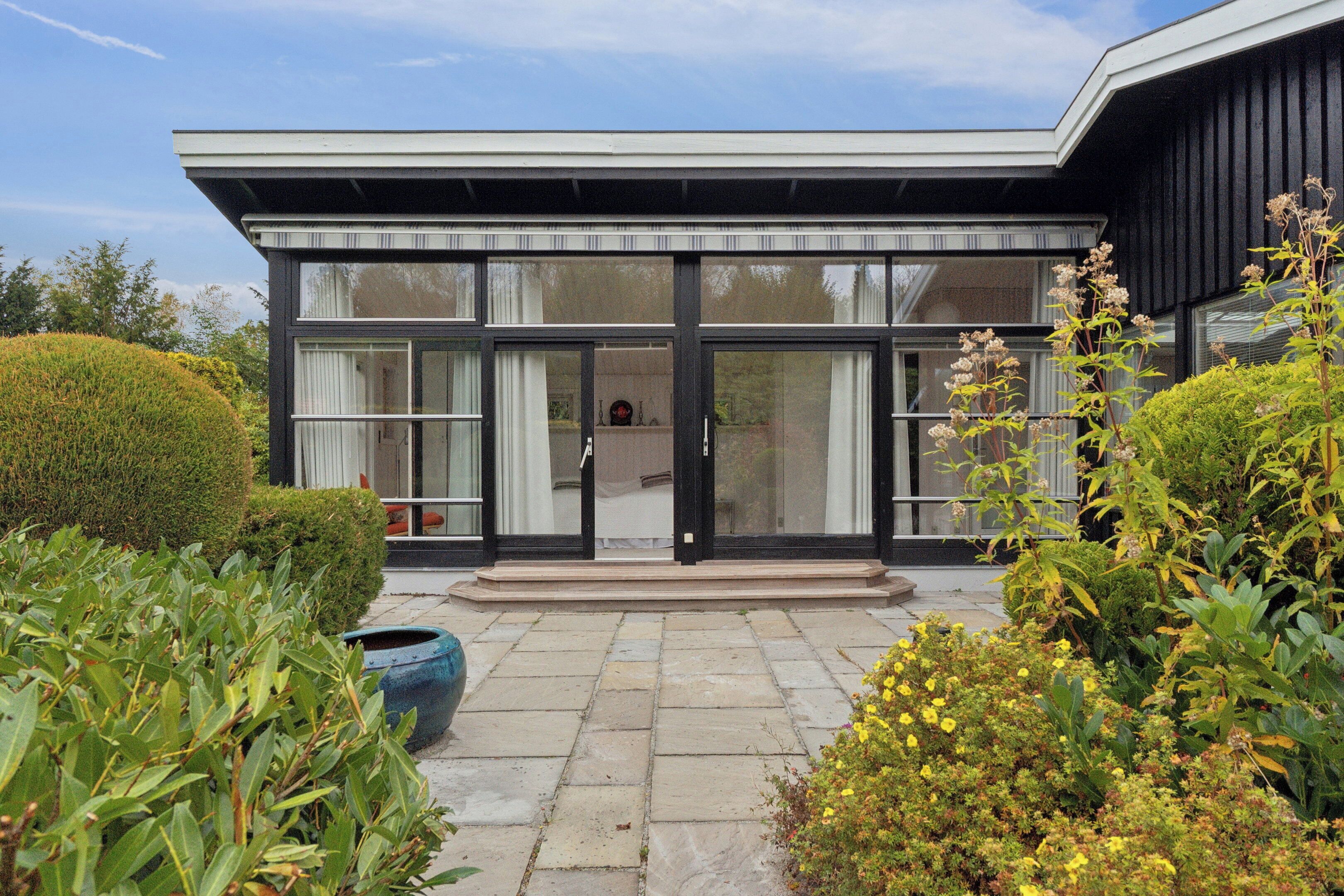 A modern building with large glass doors, a stone-paved entrance, and a well-maintained garden with various plants and flowers.