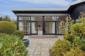 A modern building with large glass doors, a stone-paved entrance, and a well-maintained garden with various plants and flowers.