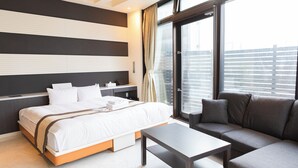 A modern hotel room with a large bed, a sofa, a small table, and a large window offering a city view. - Hotel Rima chocolat (Sapporo)