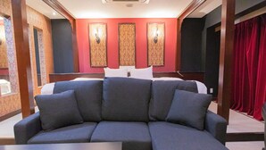 A modern hotel room with a sectional sofa, a bed with white linens, and decorative wall sconces. - Hotel Rima chocolat (Sapporo)