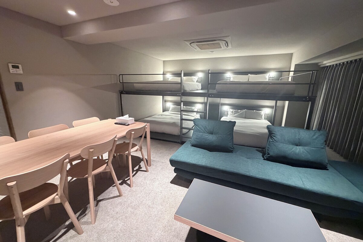 A room with bunk beds, a sofa, a dining table with chairs, and a small table.