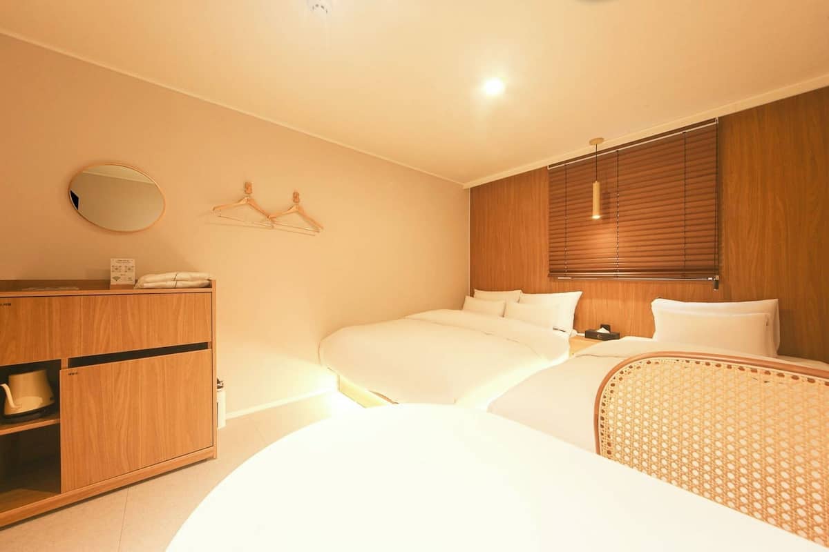 A bedroom with two beds, a wooden wardrobe, a mirror, and a hanging rack.