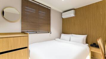 Una habitación de hotel moderna con una cama grande, paneles de madera, un espejo redondo y una ventana con persianas.