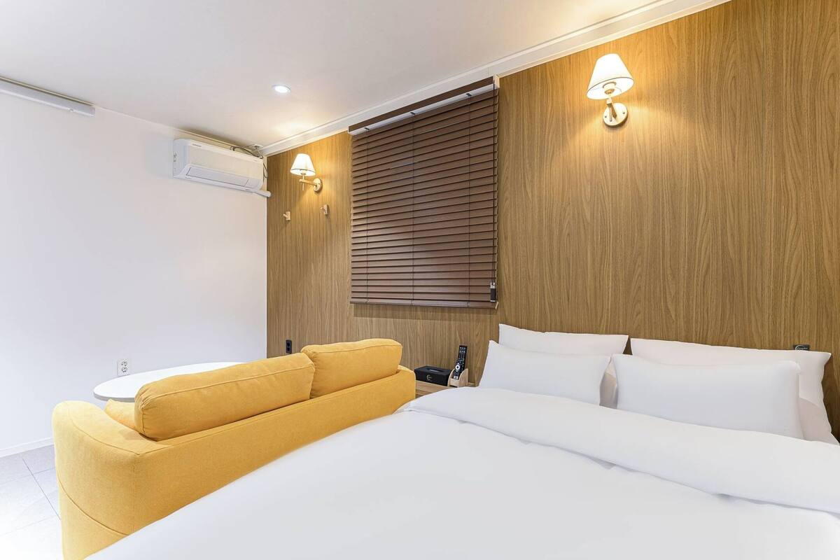 A modern bedroom with a bed, a yellow sofa, wooden paneling, and wall-mounted lights.