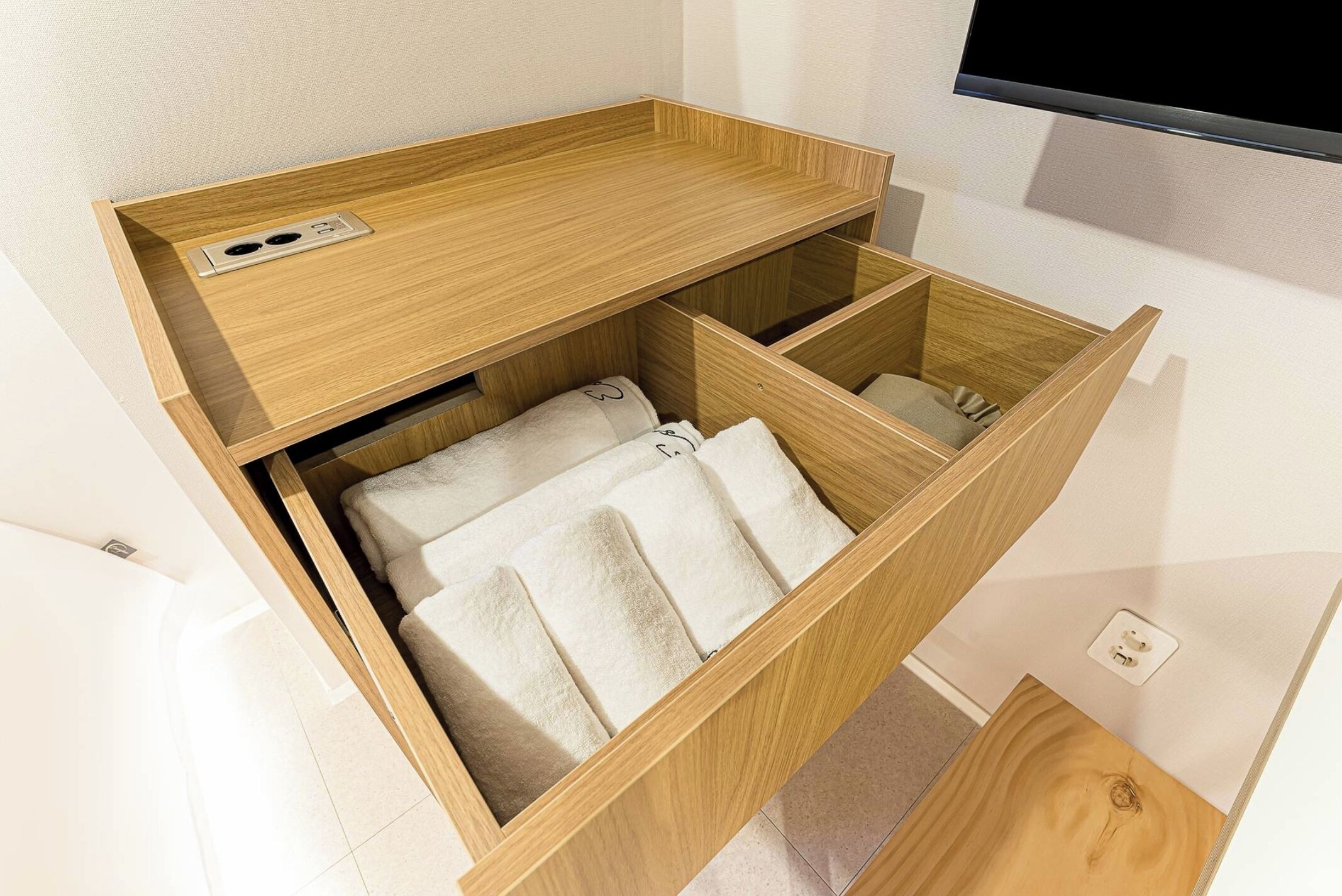 A compact wooden storage unit with a built-in electrical outlet and a foldable seating area.