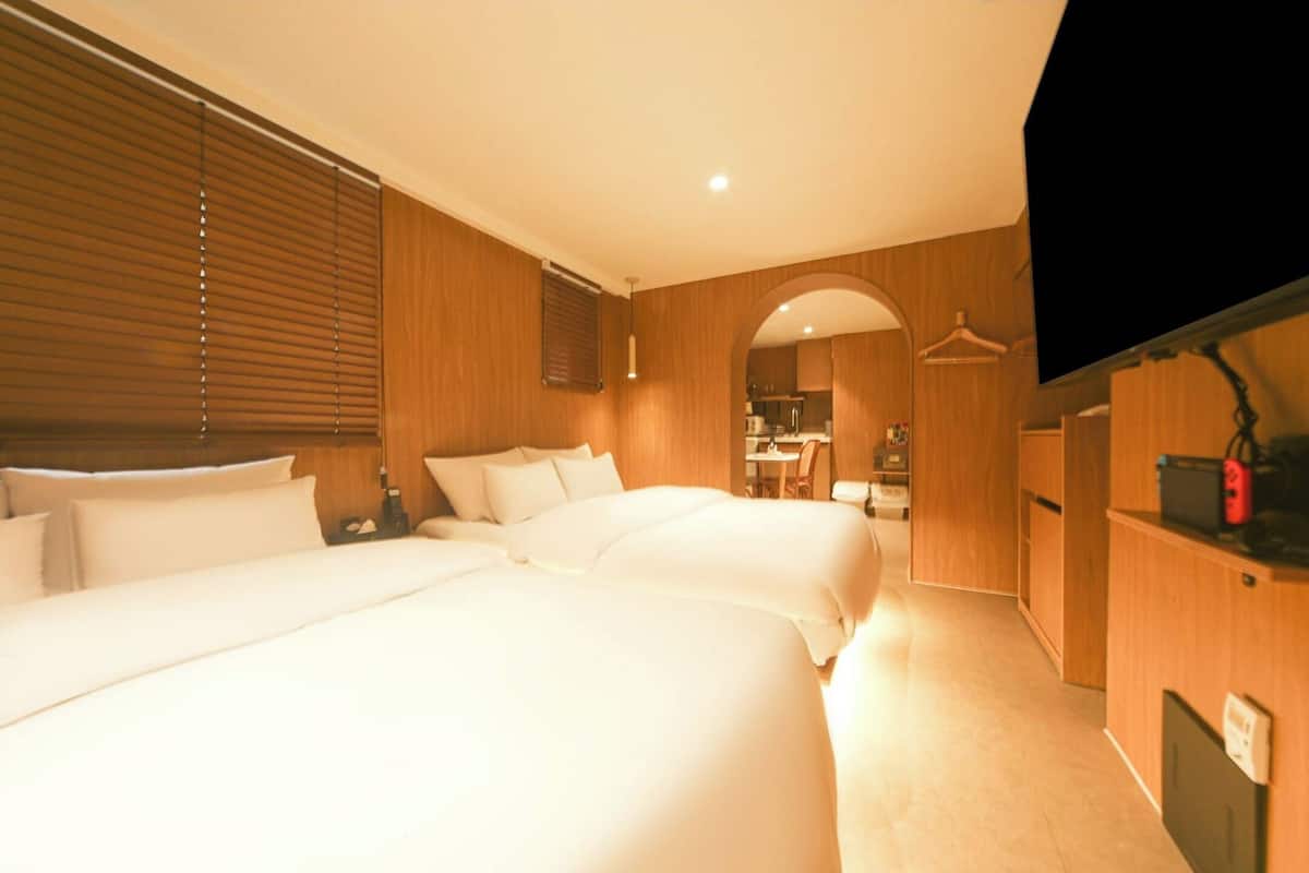 A hotel room with two beds, wooden paneling, a TV, and a kitchenette in the background.