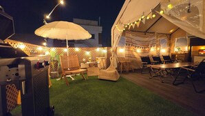 En udendørs terrasse med grill, siddepladser og lyskæder.