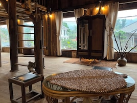 Um interior de madeira com uma mesa redonda de vime, um banco de madeira e uma janela grande com cortinas.