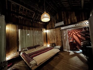 Una habitación con una cama, una lámpara colgante, techo de madera y una ventana con cortinas.
