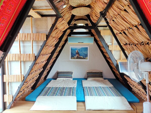 Habitación triangular con cama, almohadas, un ventilador y un cuadro en la pared.
