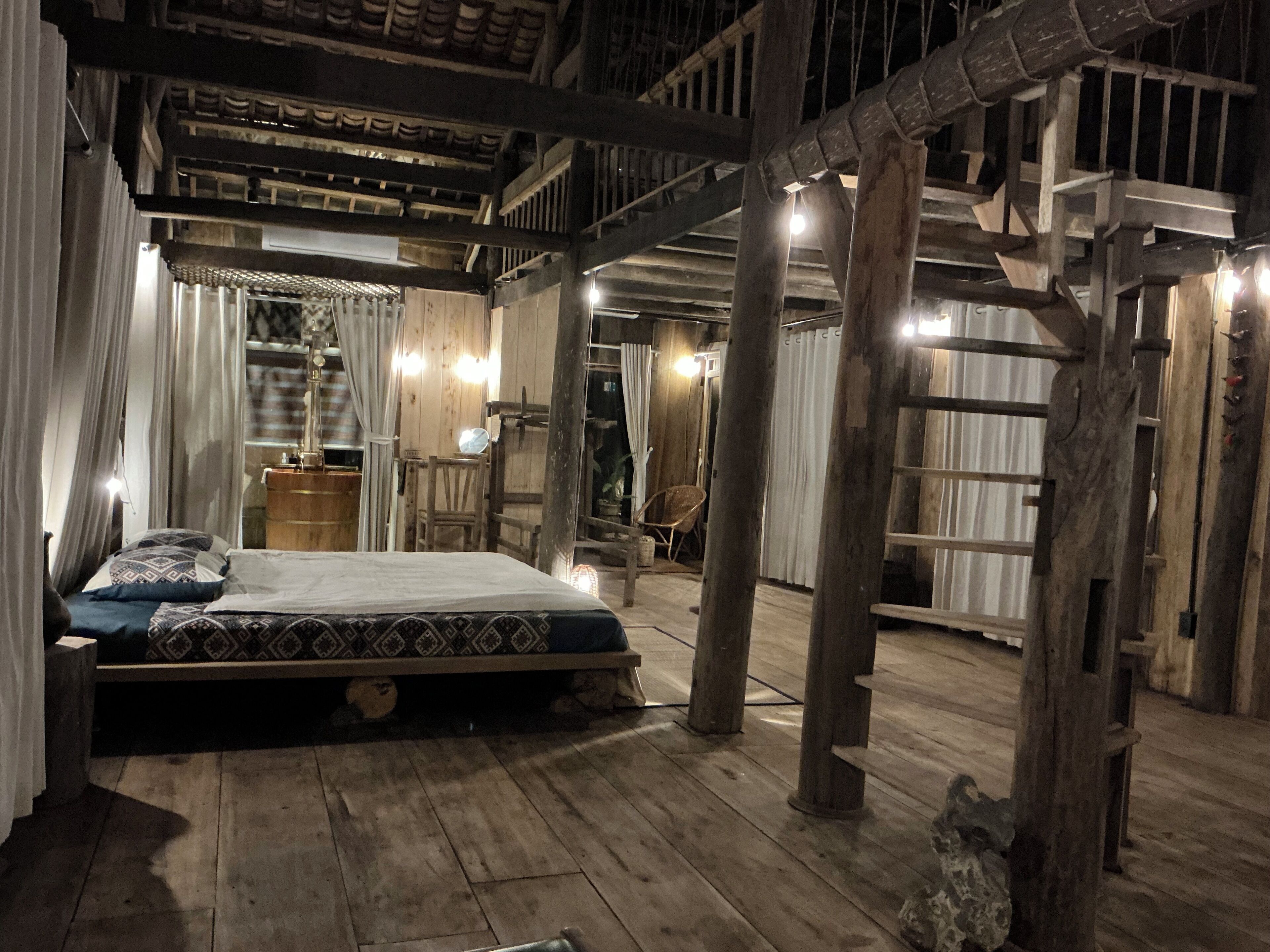 A rustic wooden room with a bed, curtains, and a ladder.