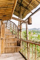 Escadaria de bambu que leva a uma área coberta com vista para a vegetação e montanhas.