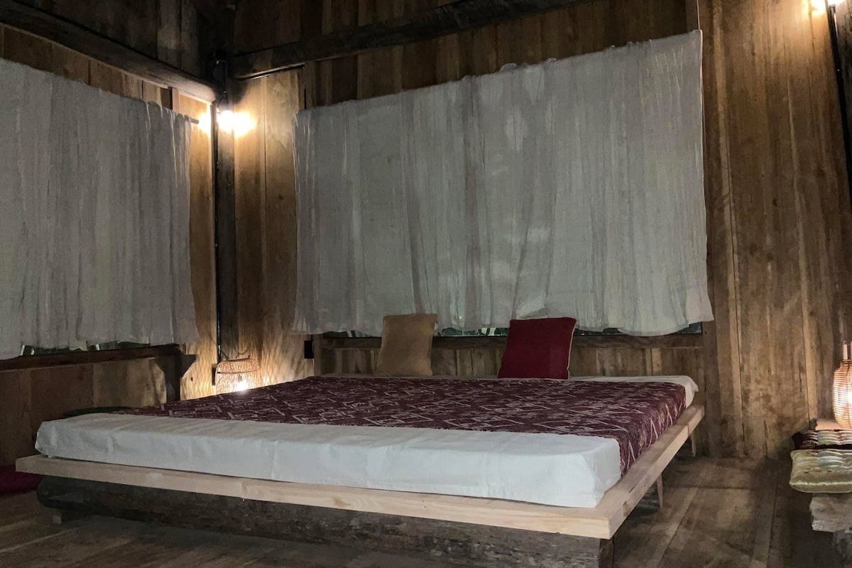 Una habitación de madera con una cama, cortinas y una mesita de noche.