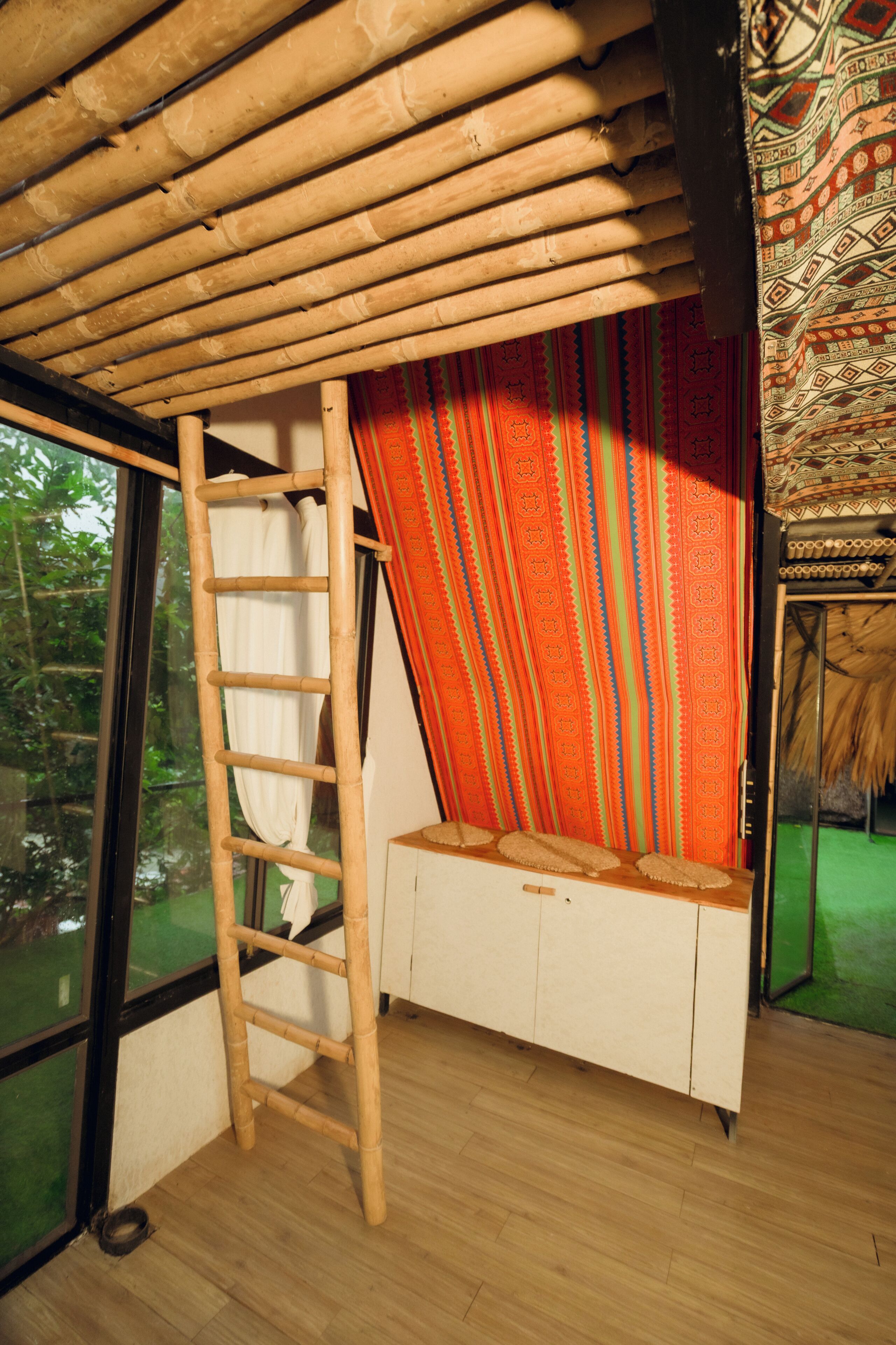 Een kamer met een houten ladder, een bank met een gestreept kussen en een raam met uitzicht op groen.